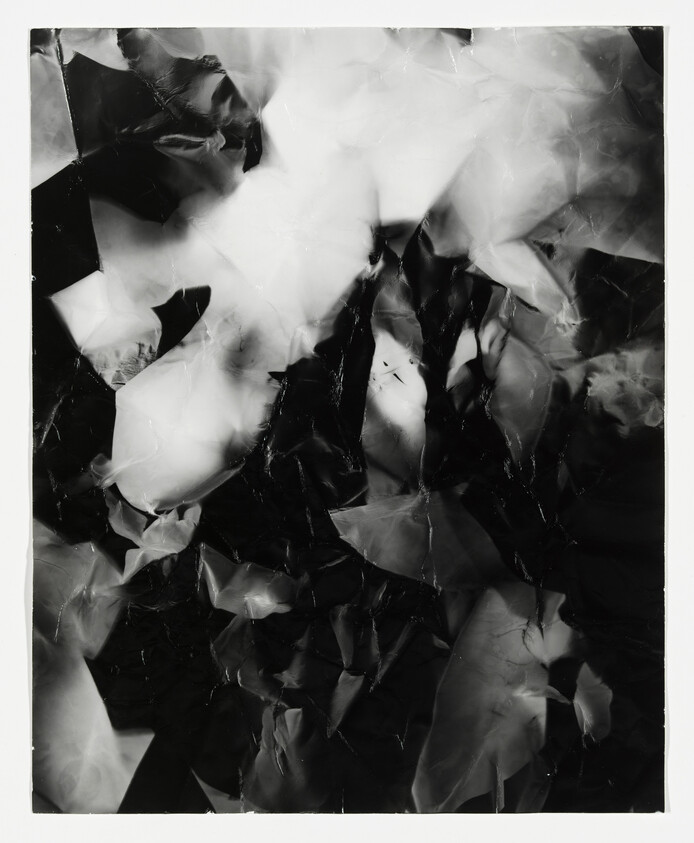 A black and white abstract image featuring a chaotic arrangement of crumpled and overlapping shapes that create a dynamic interplay of light and shadow.