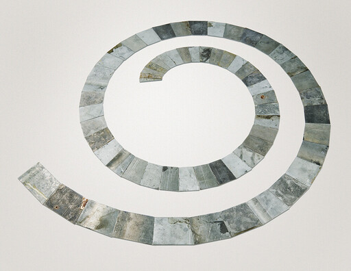 A spiral of weathered rectangular metal tiles arranged on a plain white background.
