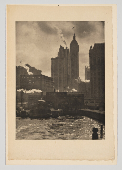 Riverfront with boats and steam rising against tall city buildings under a cloudy sky.