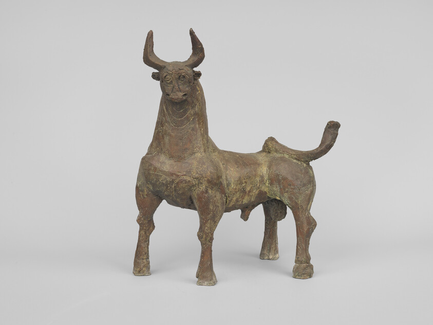 Bronze sculpture of a horned bull standing on four legs with a raised tail.