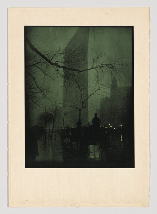 A horse-drawn carriage and driver silhouetted on a rainy city street in front of the Flatiron Building.