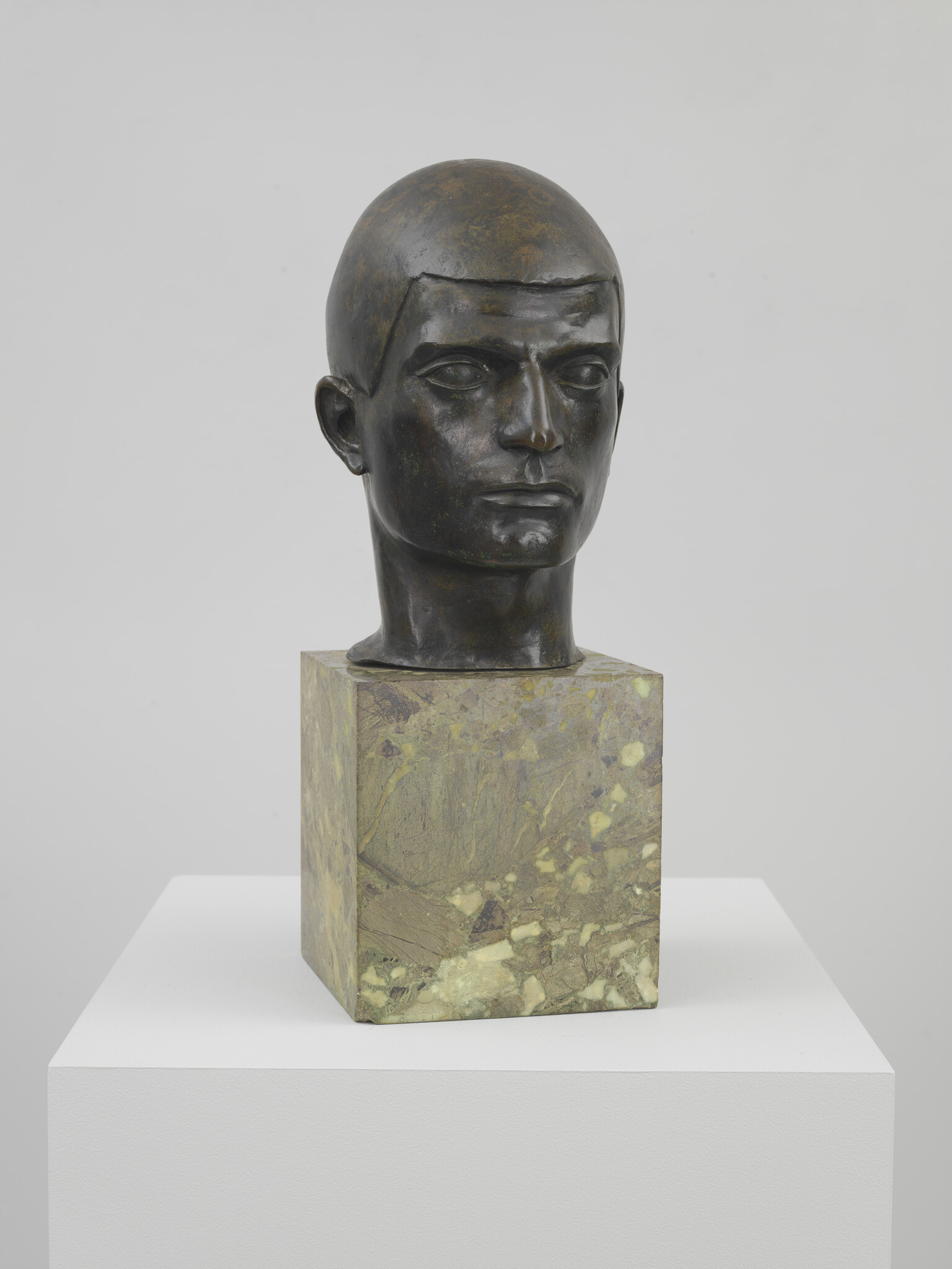 Bronze bust of a young man with short hair mounted on a green marble block.
