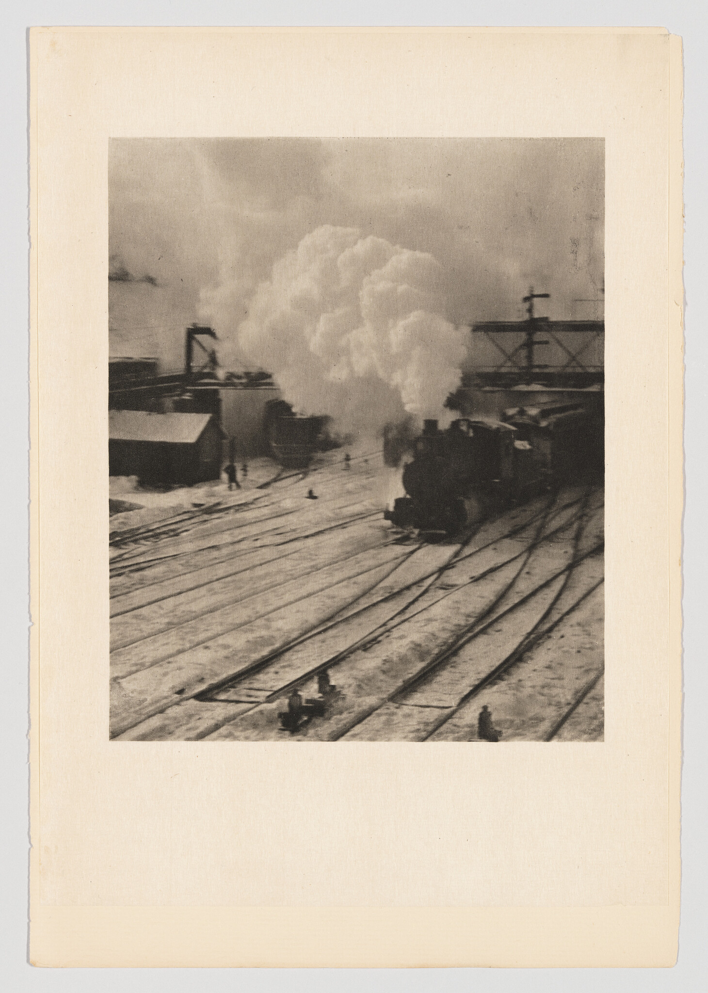 A steam locomotive releases a large plume of steam while moving through a snowy rail yard.