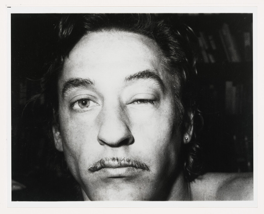 Close-up of a man with a small mustache winking one eye directly at the camera.