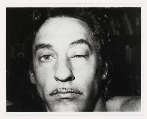 Close-up of a man with a small mustache winking one eye directly at the camera.
