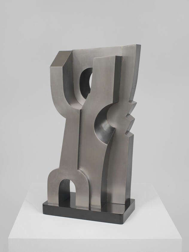Abstract polished metal sculpture with geometric cutouts and smooth planes standing on a white pedestal.