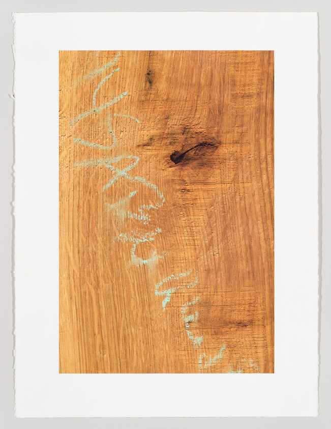 A wooden board with pale blue chalk scribbles running diagonally across its grain.