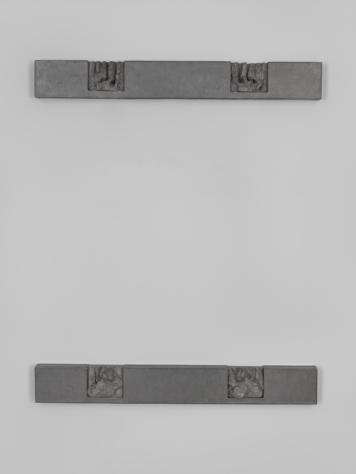 Two horizontal metal bars with small square reliefs mounted on a pale wall, top and bottom.
