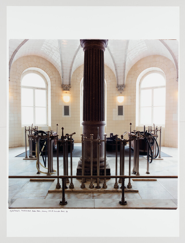 Central cast-iron column surrounded by vintage pump controls in a tiled pump room with arched windows.