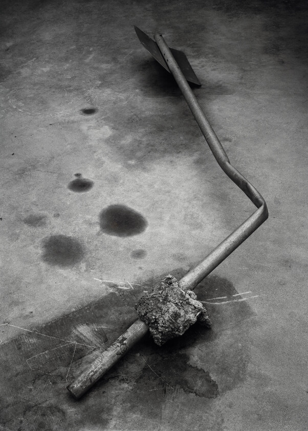 A bent metal signpost with a chunk of concrete attached lies on stained pavement.