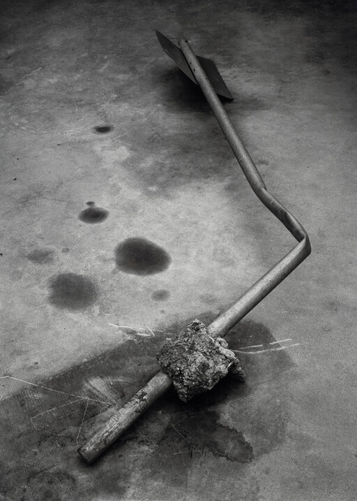 A bent metal signpost with a chunk of concrete attached lies on stained pavement.