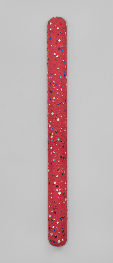 A long red foam stick covered in multicolored sequins on a gray background.