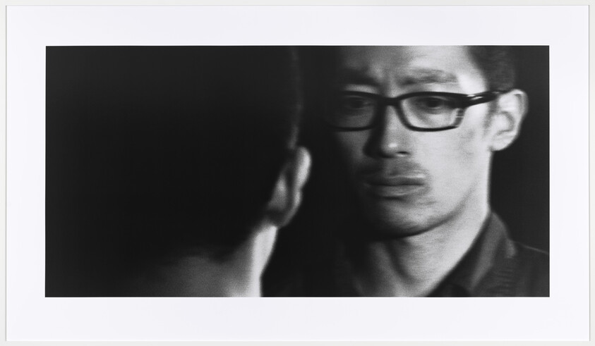 Man wearing glasses stares intently at another person across from him.
