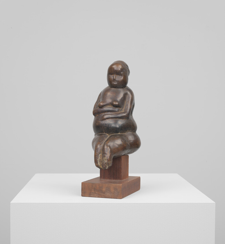 A small bronze sculpture of a seated woman with folded arms on a wooden base.