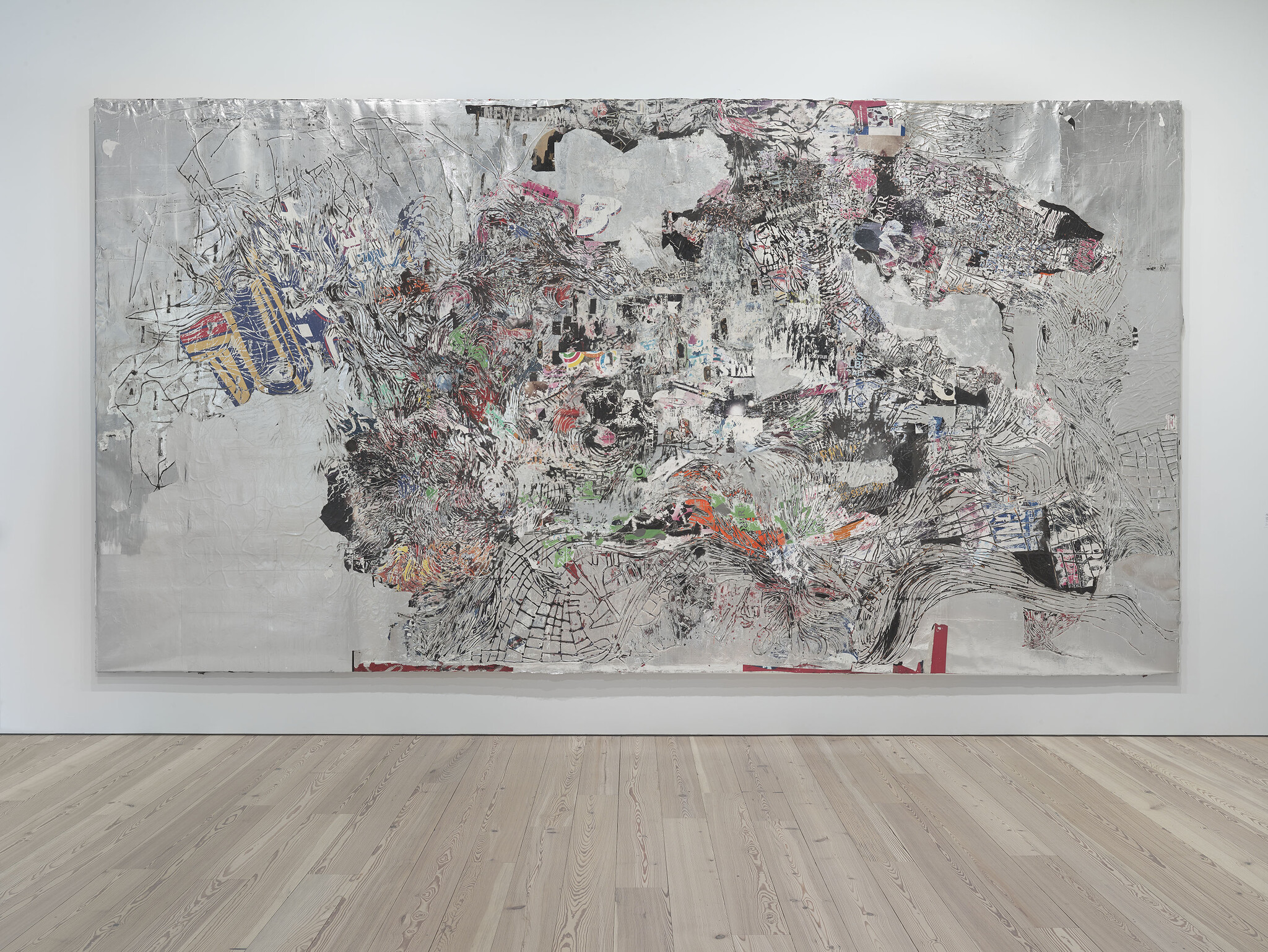 Large abstract mixed-media artwork with silver background and chaotic textured collage displayed in a gallery.