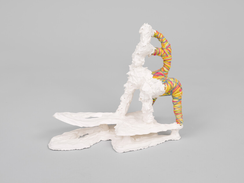 A white textured abstract sculpture with a colorful twisted band rests on flat layered bases.