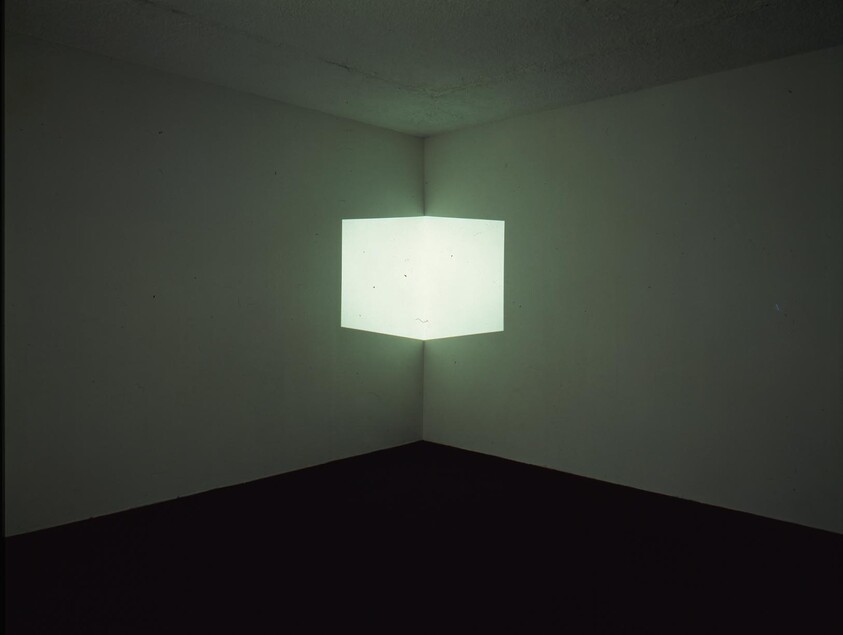A glowing white cube projection appears suspended in the corner of a dim, empty room.