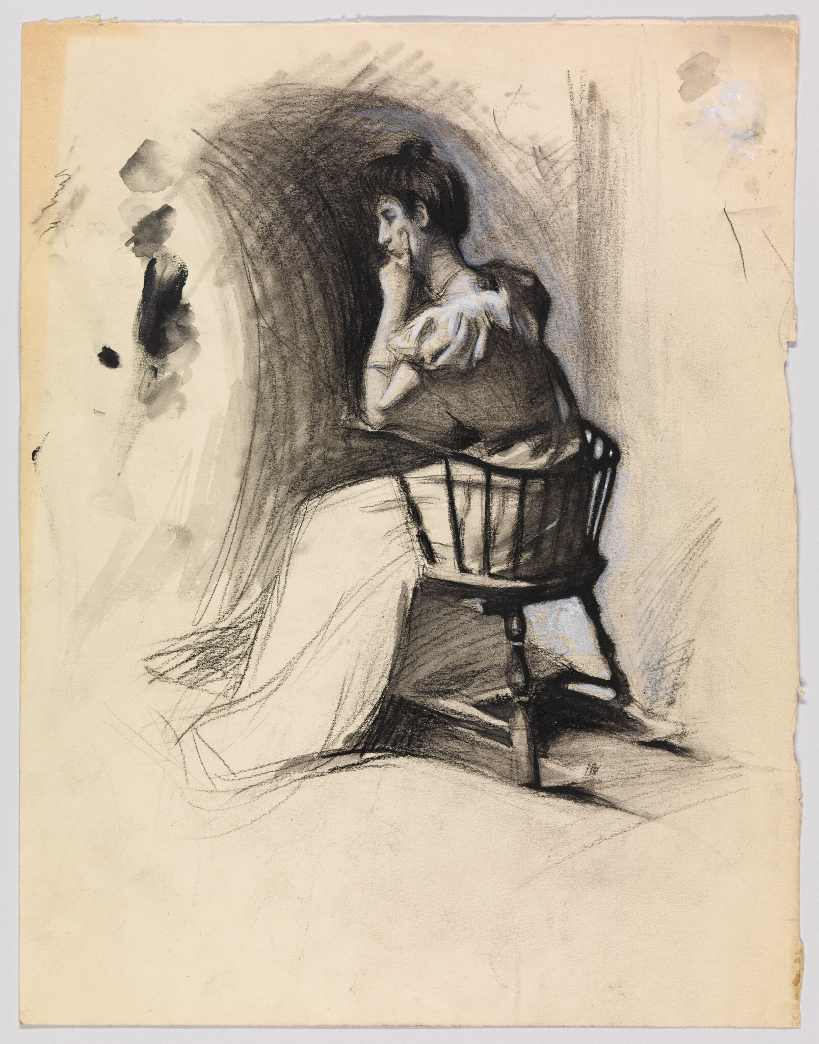 A woman sits on a wooden chair resting her head on her hand in thought.
