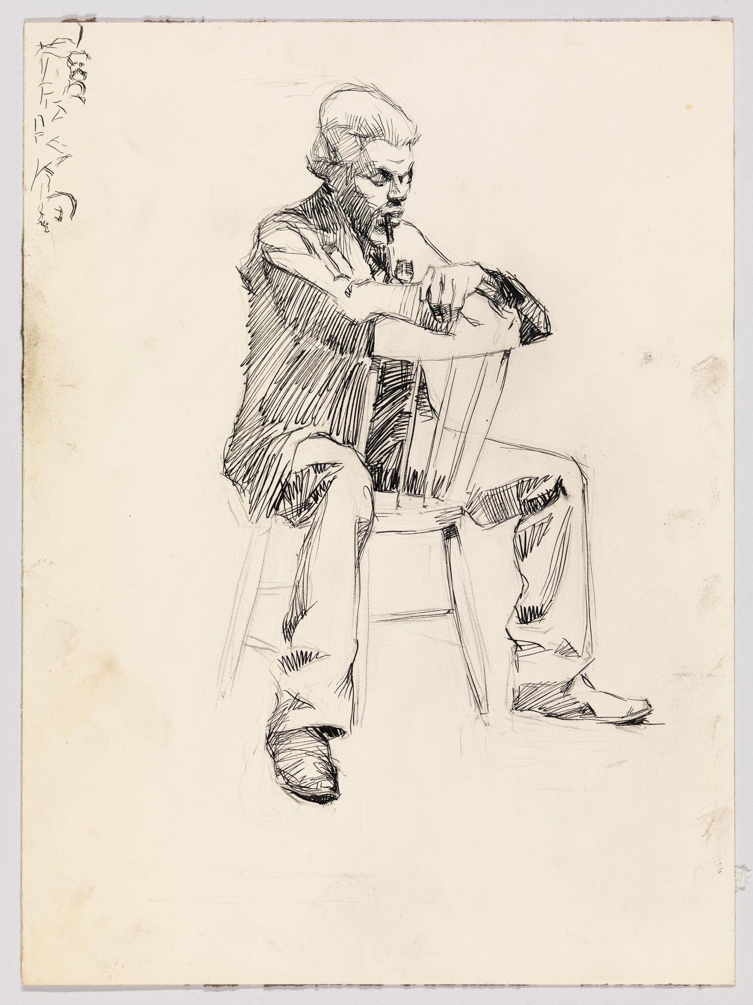 Man sits backward on a wooden chair resting his arms on the chair back and looking down.