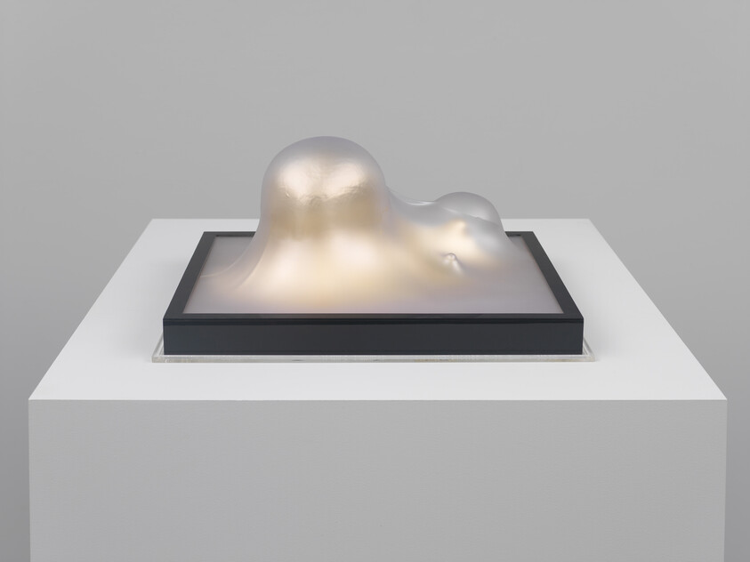 Translucent, glowing gelatinous sculpture with smooth rounded forms displayed on a white pedestal.