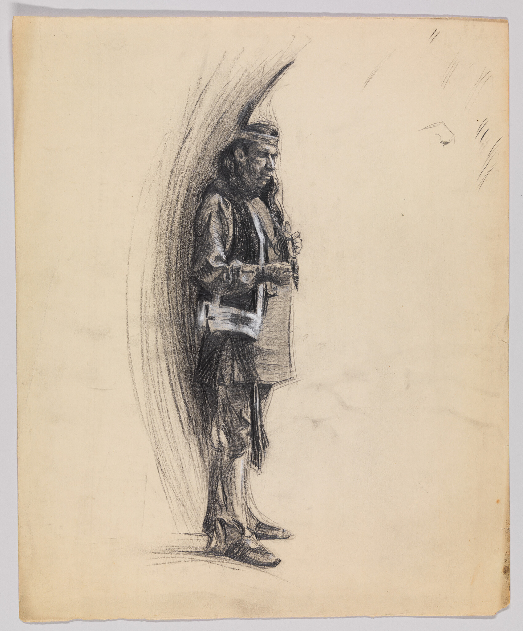 A standing man in traditional clothing plays a small flute while leaning against a shaded background.