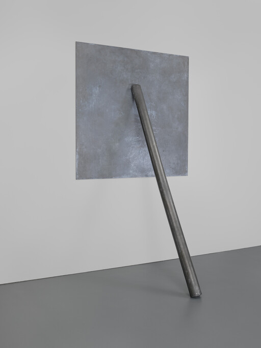 A long metal pole leans diagonally against a square metal panel mounted on a white wall.