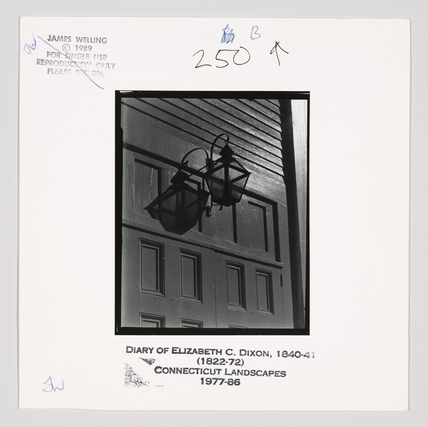 Two old-fashioned lanterns mounted on the exterior wall above paneled doors, cast strong shadows.