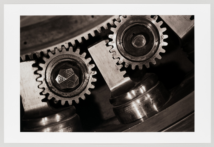 A sepia-toned photograph showing a close-up of interlocking metal gears with intricate details, reflecting the precision of mechanical engineering.