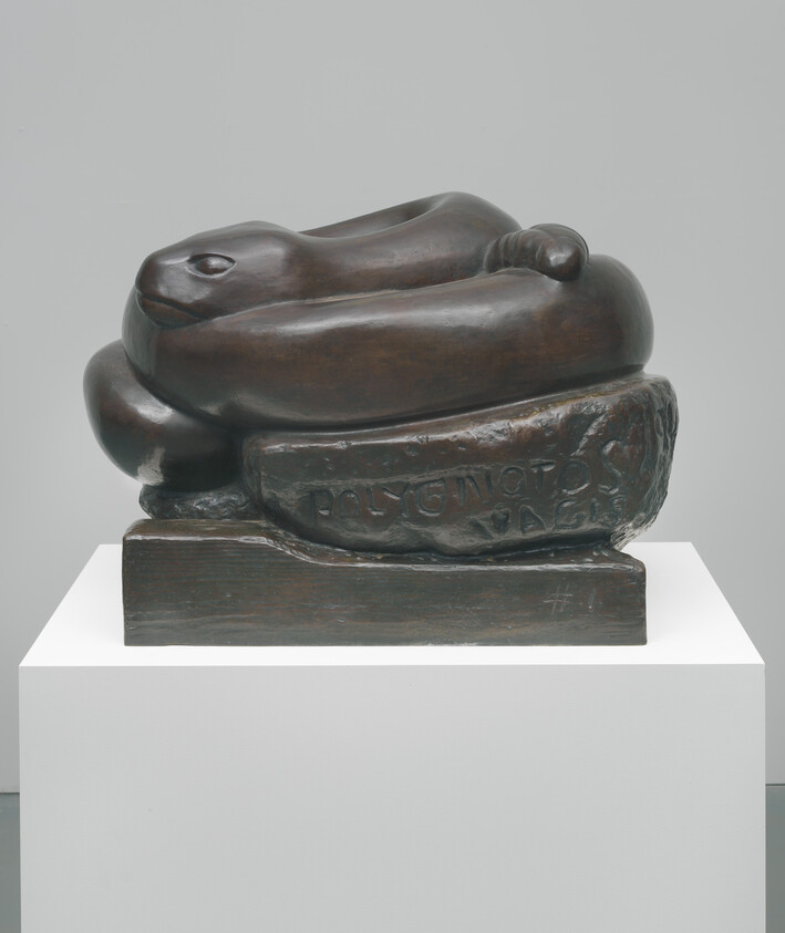 Bronze sculpture of a coiled snake resting on a carved rectangular base on a pedestal.