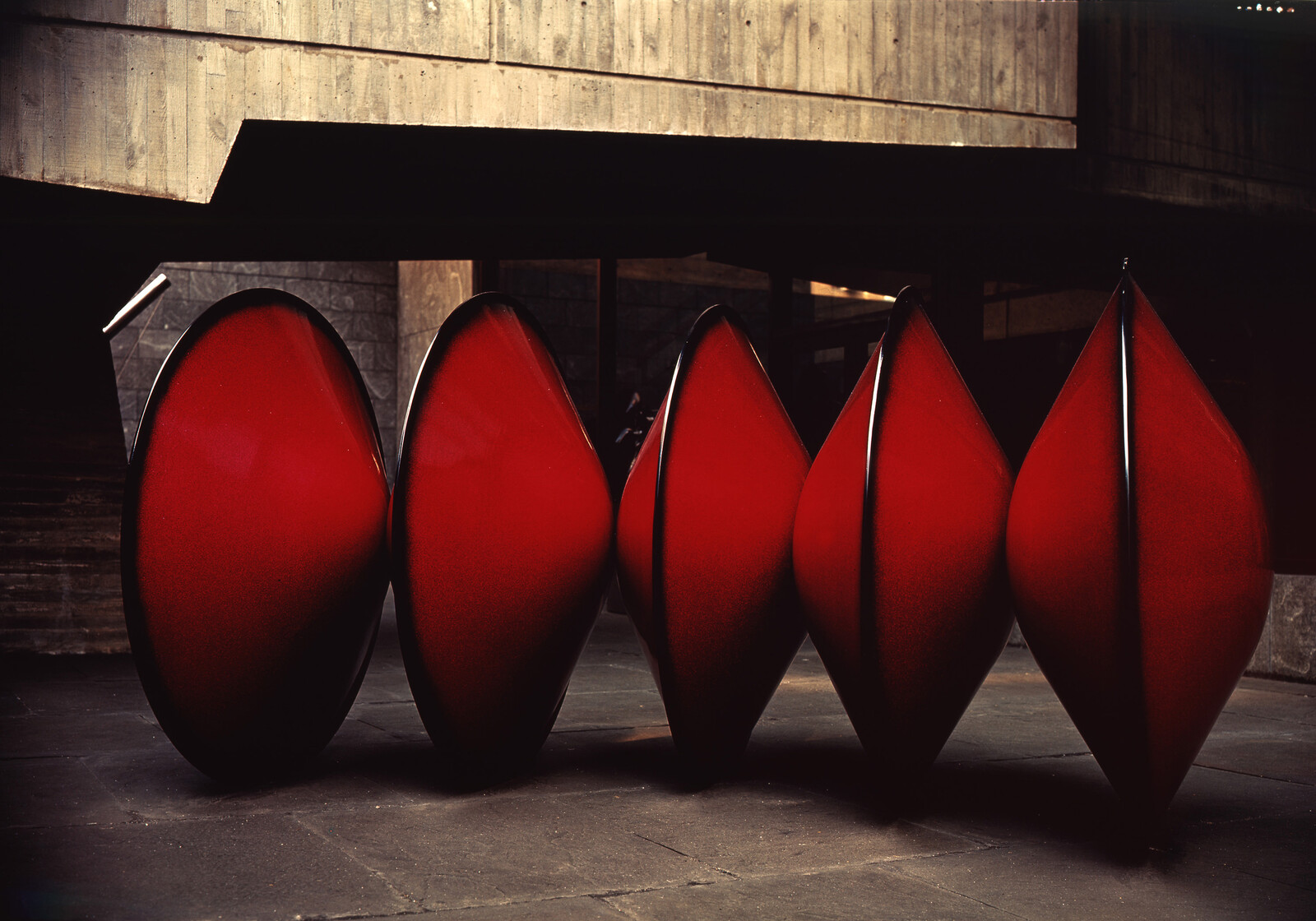 Five red canoes standing upright on their edges under a concrete overhang.