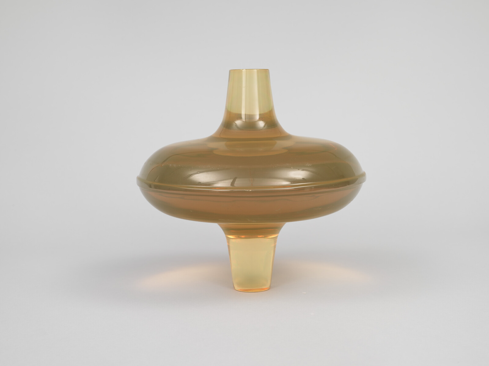 A translucent amber glass spinning-top shaped vessel with a rounded body and tapered stem.