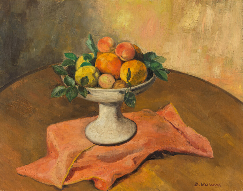 Pedestal bowl of oranges, peaches, and leaves sitting on a pink cloth on a wooden table.