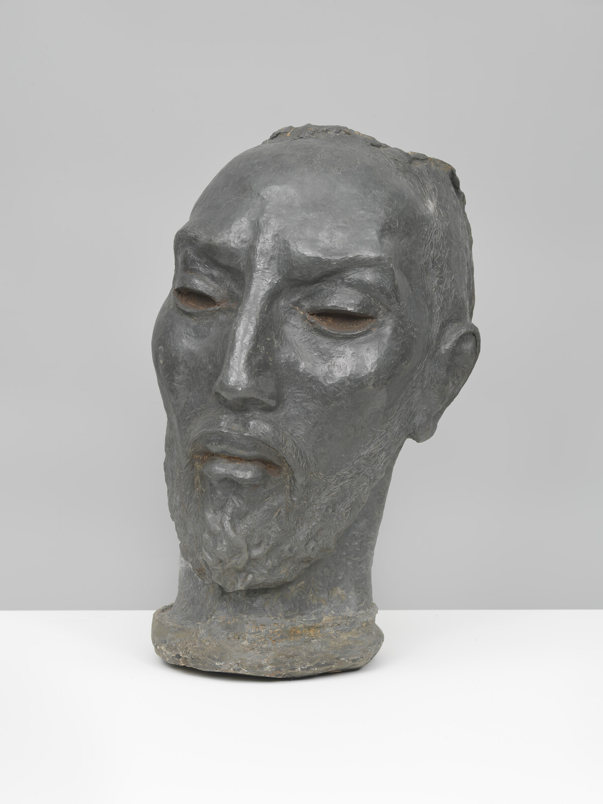 Sculpted gray bust of a bearded man with closed eyes and a calm expression.