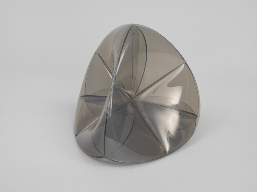 A translucent gray plastic sculpture with folded, star-like creases resting on a plain surface.