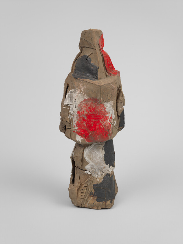 Abstract standing clay sculpture with rough brown surface and a prominent red circular paint mark.