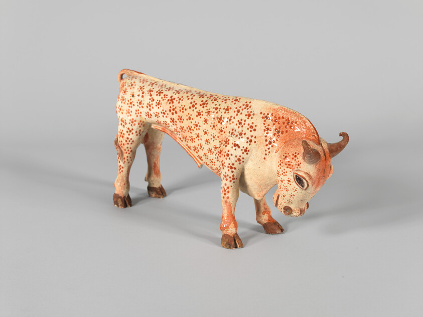 A small ceramic spotted bull sculpture stands with its head lowered and one horn curled.