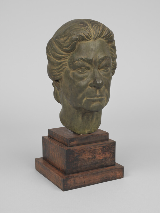 Bronze bust of an older woman's head with detailed features mounted on a wooden pedestal.