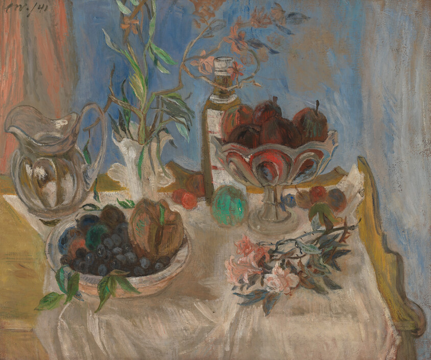 A table with bowls of fruit, a pitcher, a bottle, and flowers on a white cloth.
