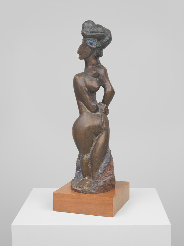 Bronze stylized standing female figure with hands behind her back and a painted eye.