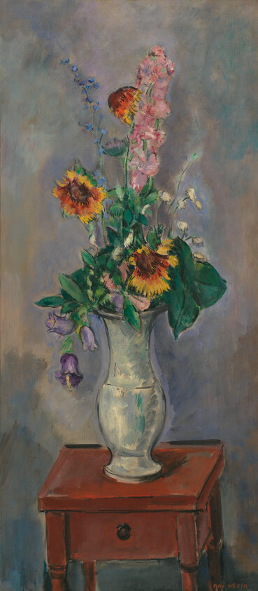 A tall ceramic vase holds sunflowers and mixed wildflowers on a small wooden table.