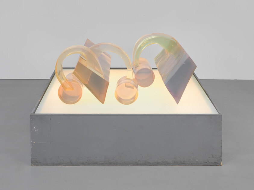 Translucent curved glass tubes and angled panels rest on a glowing rectangular pedestal.