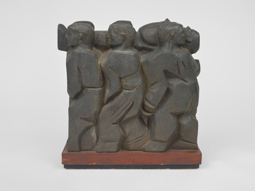 Carved dark wooden sculpture showing three stylized figures walking side by side on a base.