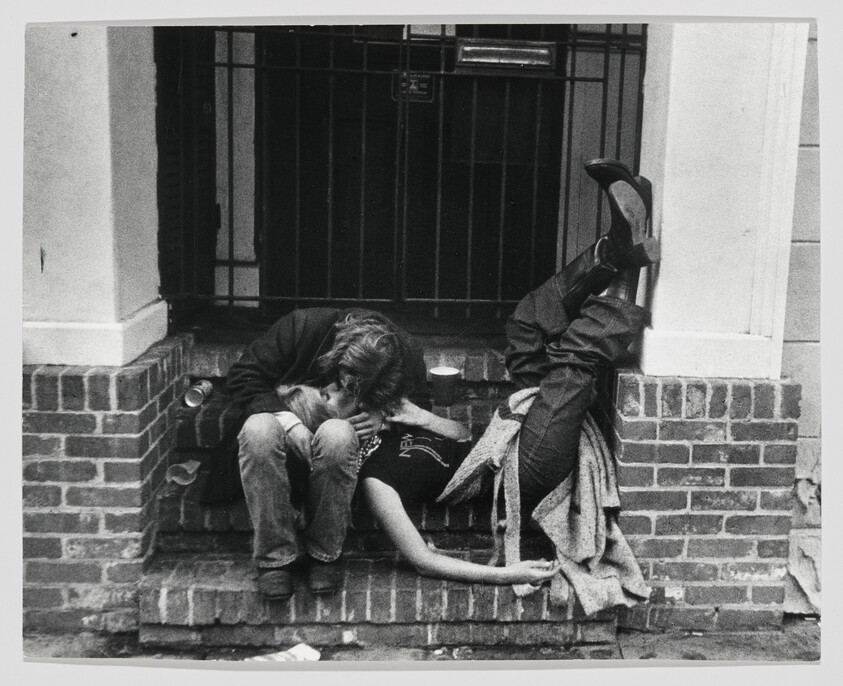 A couple sits on brick steps kissing, one person leaning back with legs raised.