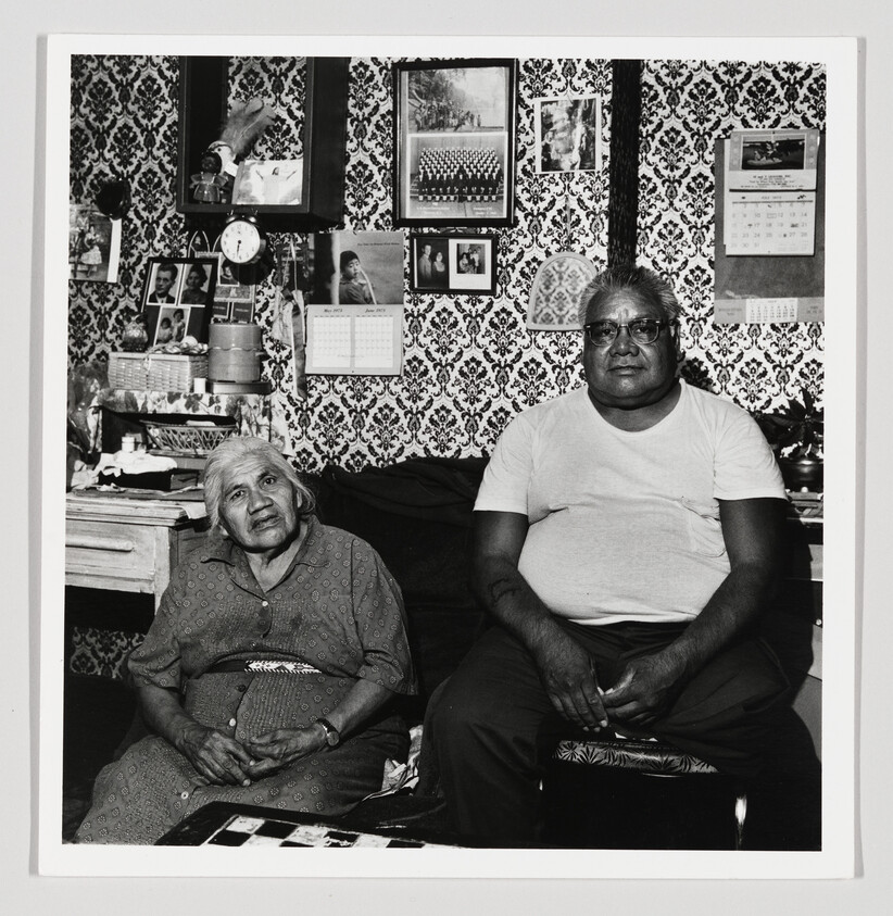 An elderly woman and middle-aged man sit side by side in a patterned living room.
