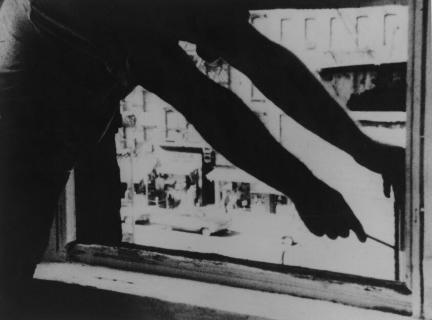 Person reaching through an open window with both arms, holding a tool, with a street scene outside.