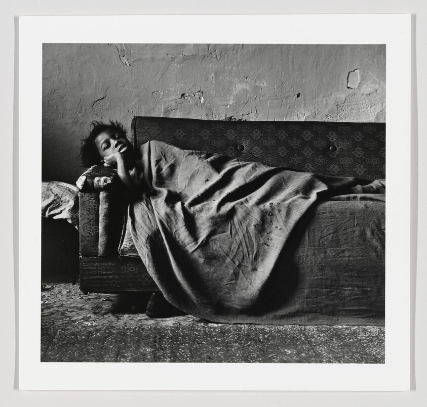 A child lies wrapped in a blanket on a worn couch in a simple room.