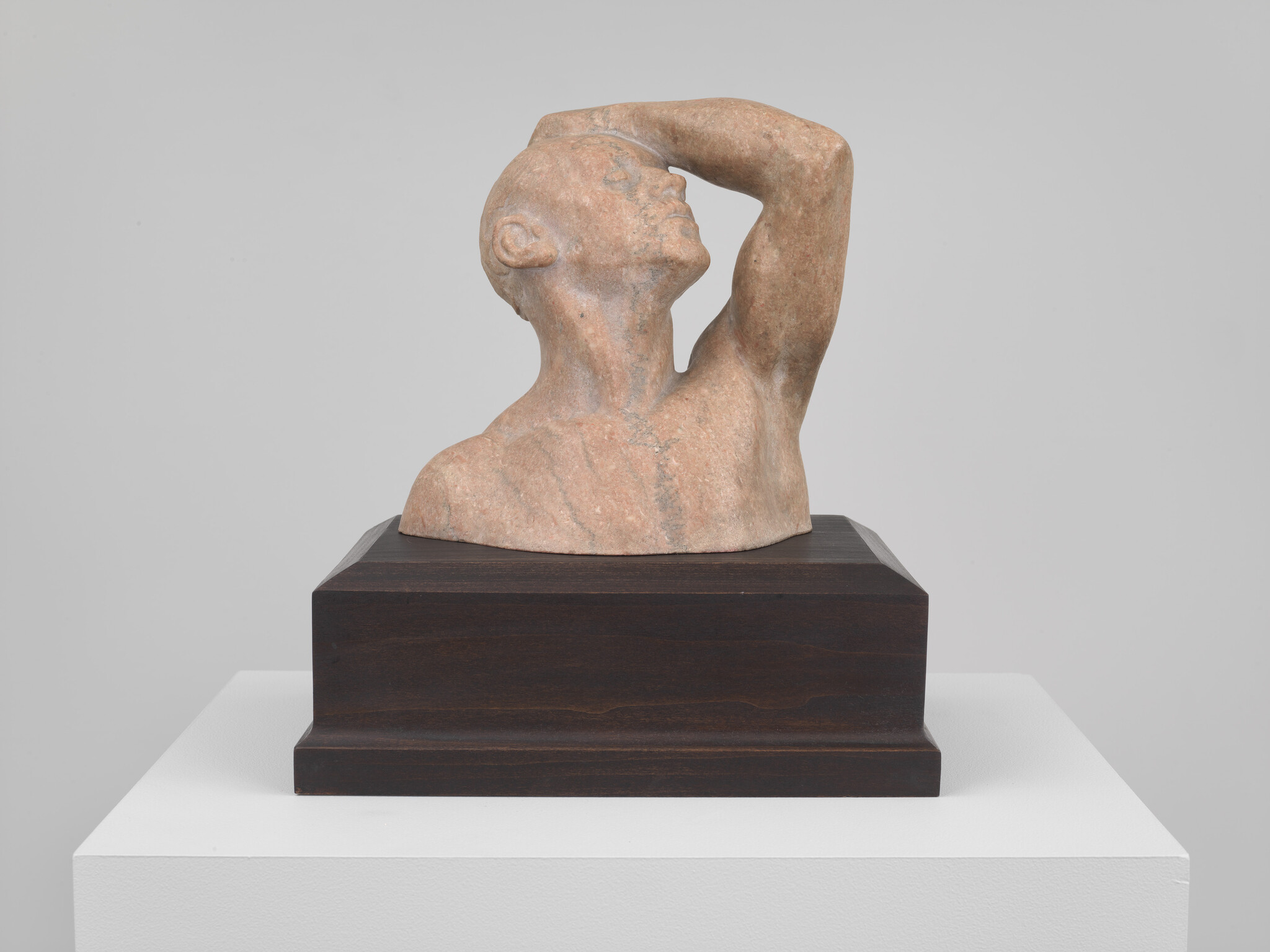 A stone sculpture of a man looking upward with one arm raised over his forehead.