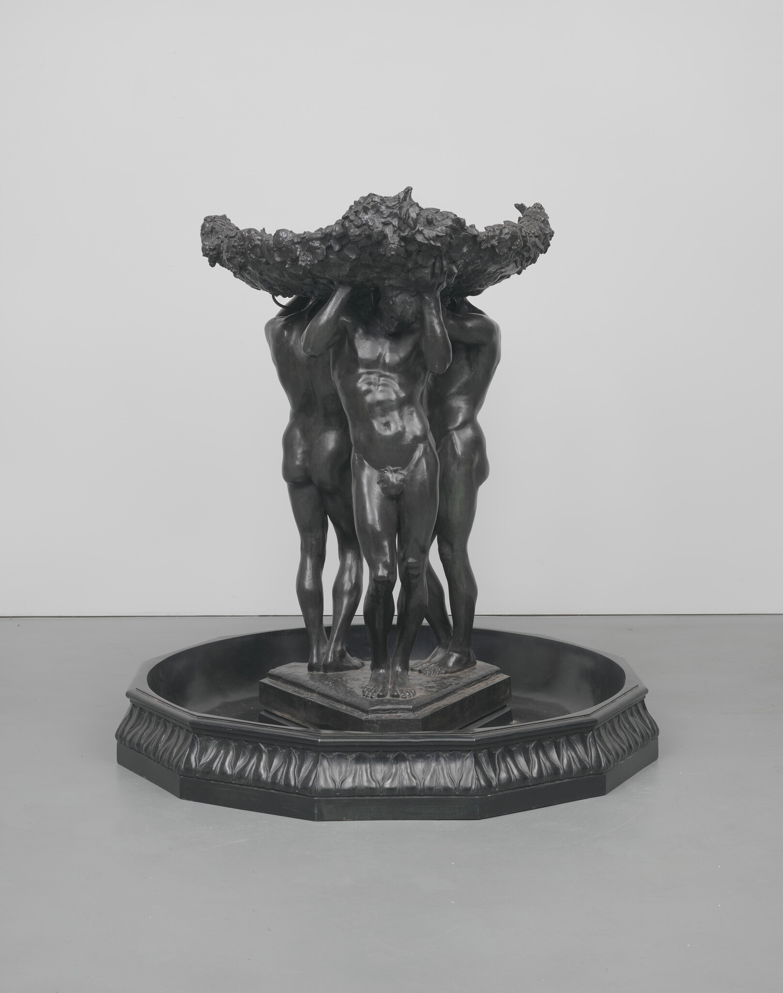 Four nude male figures stand in a circle holding a large ornate bowl above their heads.