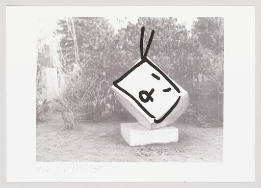 Tilted stone cube sculpture on a pedestal outdoors with a simple drawn face overlay.