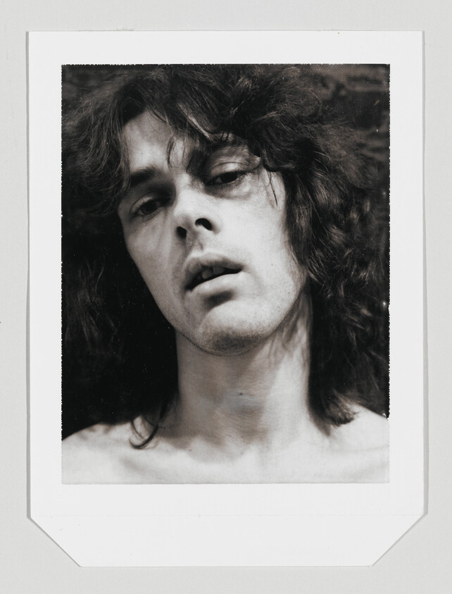 Young person with long messy hair looks upward with slightly open mouth and bare shoulders.